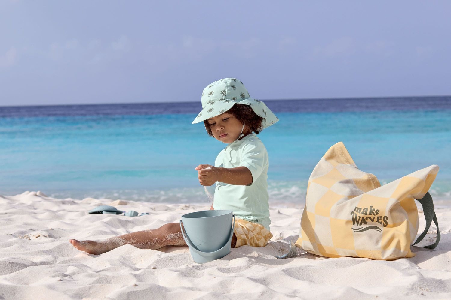 Mädchen spielt am Sandstrand, es trägt die Badehose "Check Pattern" in pastellgelb und weiss von LÄSSIG