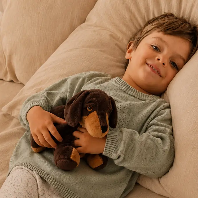 Ein kleiner Junge kuschelt im Bett mit dem Wärmestofftier Dackel von Habibi Plush.