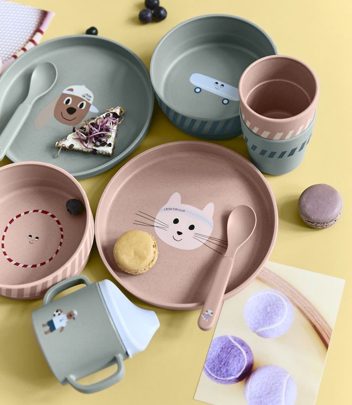 Auf einem gelben Tisch sind die Geschirrsets Tiny Team Dog in grün uund Tiny Team Cat in rosa ausgebreitet