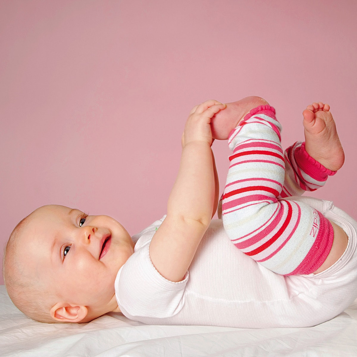 Baby mit Hoppediz-Stulpen geringelt in weiss, rosé und pink