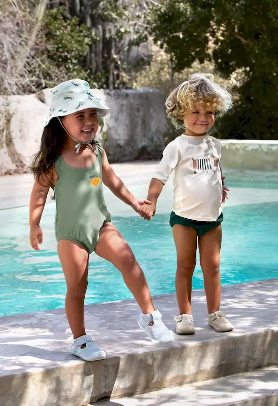 2 Kinder stehen am Poo. Das linke trägt das Lässig UV-Shirt Kurzarm Beach Dog, das linke einen grünen Badeanzug und Sonnenhut.