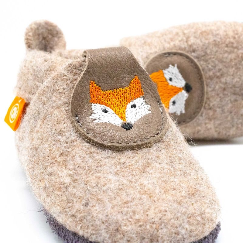 Detailansicht eines beigen Kinderhausschuhs aus Wolle mit Lederlasche, bestickt mit einem Fuchsgesicht