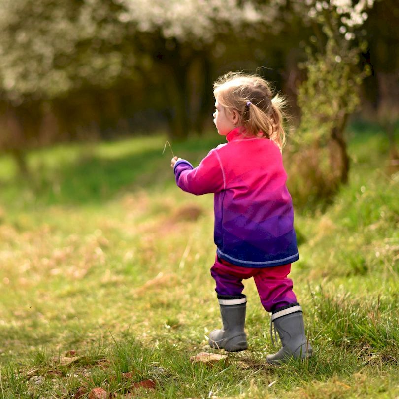 Kleines Mädchen auf der Wiese, sie trägt die Wamu Fleecejacke Mosaic Purple