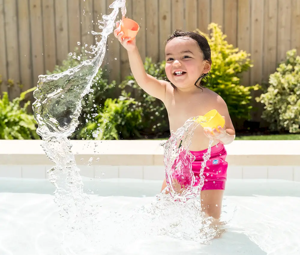 Mädchen in einem Pool trägt eine neonpinkfarbene Badewindel und spritzt fröhlich mit Wasser