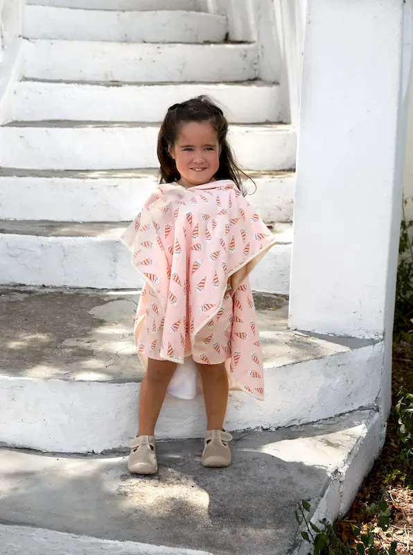 Mädchen auf einer Treppe, sie trägt einen Lässig UV-Beach Poncho Ice Cream Pale Pink.