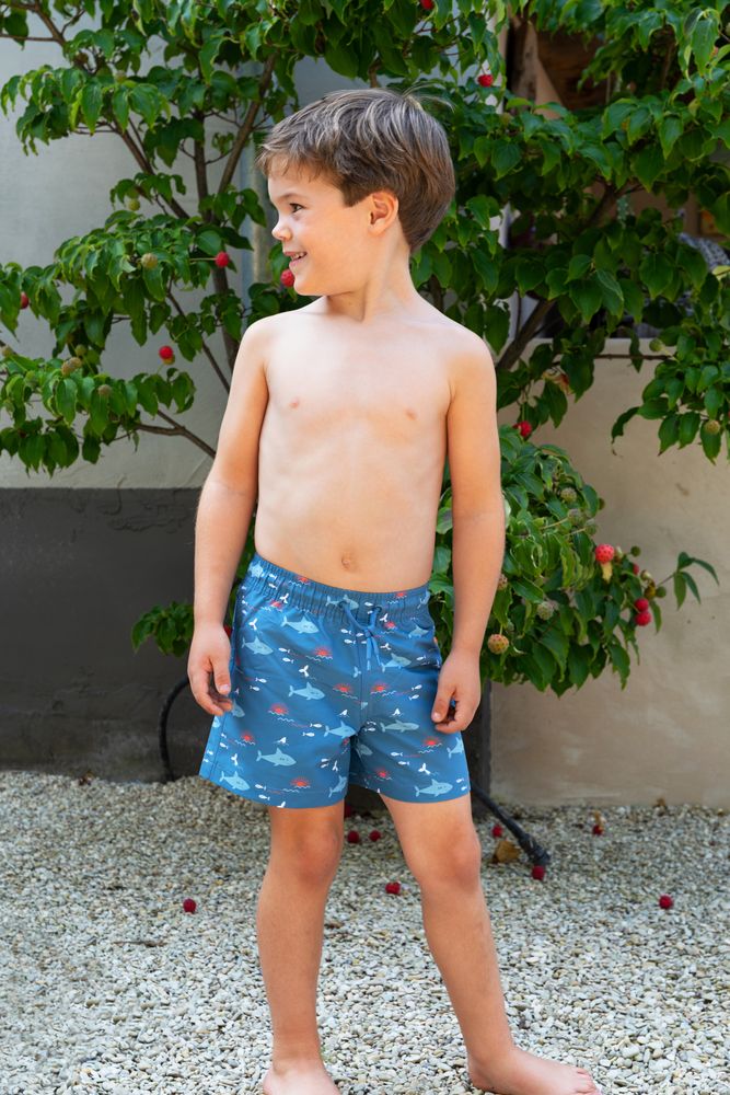 Junge, der die blaue Badehose "Shark" mit den freundlichen Haien von Fresk trägt