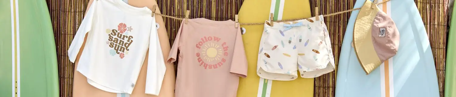 UV-Shirts, Badehose und Sonnenhut von Lässig an einer Leine vor bunten Surfbrettern.