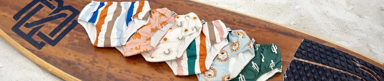 Bunte Schwimmwindeln von Lässig auf einem braunen Surfbrett, das auf dem Strand liegt.