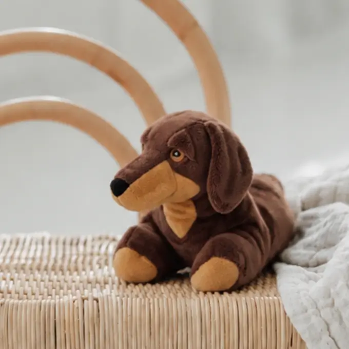 Das Wärmekuscheltier Dackel von Habibi Plush liegt auf einem Stuhl.