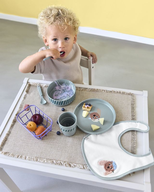 Ein kleiner blonder Junge sitzt an einem Kindertasch und isst Zvieri vom Geschirrset Tiny Team Dog von LÄSSIG