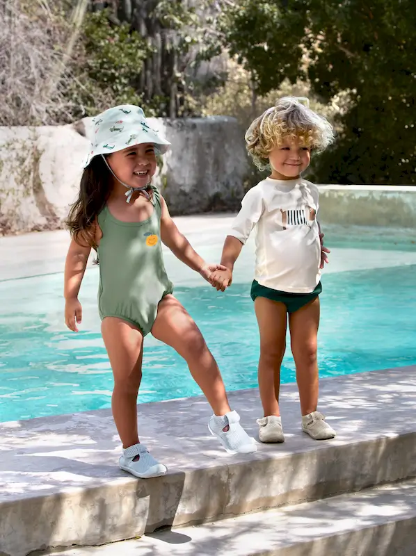 Zwei Kinder stehen am Pool. Das Mädchen trägt einen Badeanzug und denUV-Sonnenhut Ice Cream Truck von Lässig.